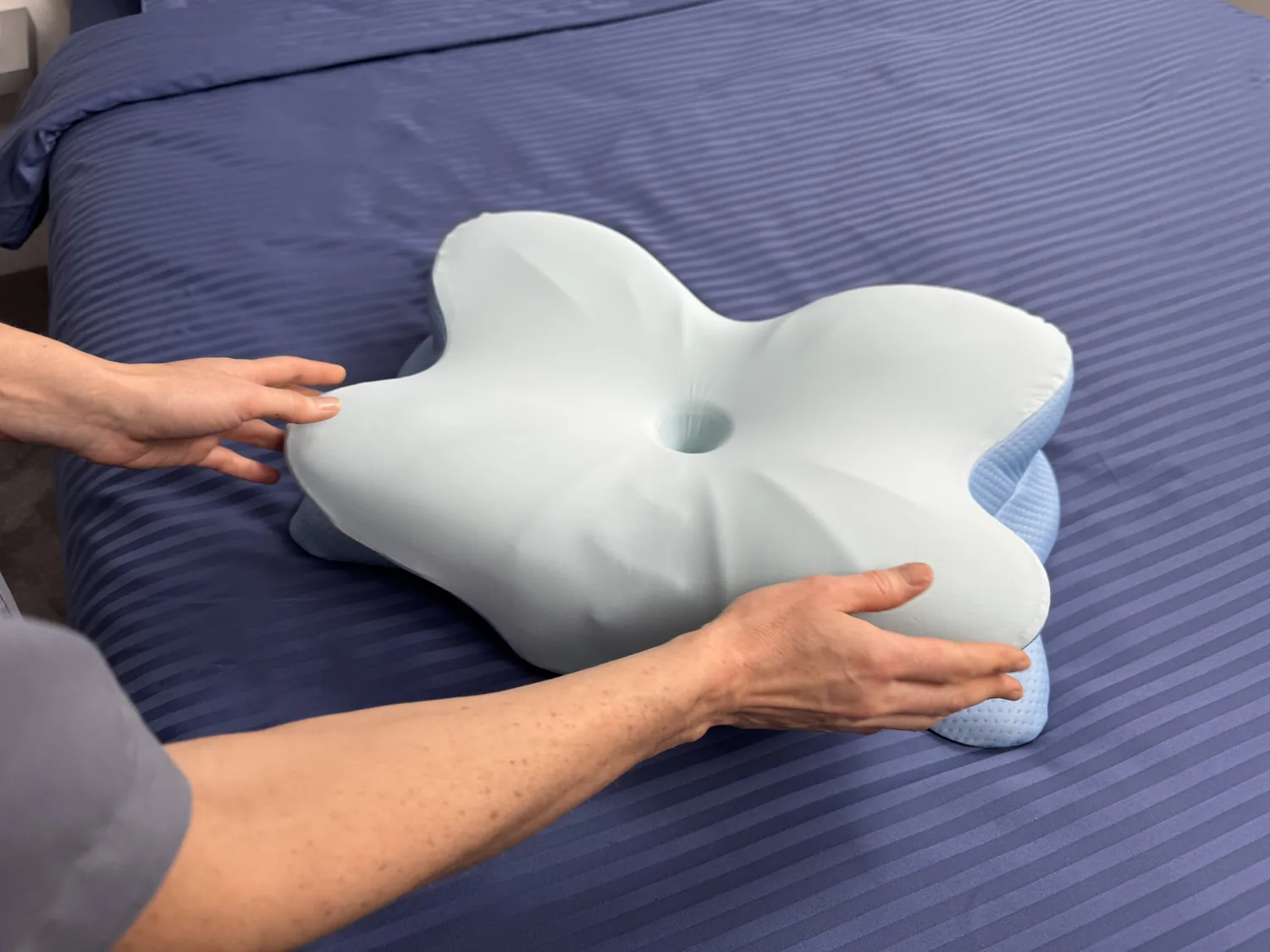 Hands positioning a contoured pillow on a bed